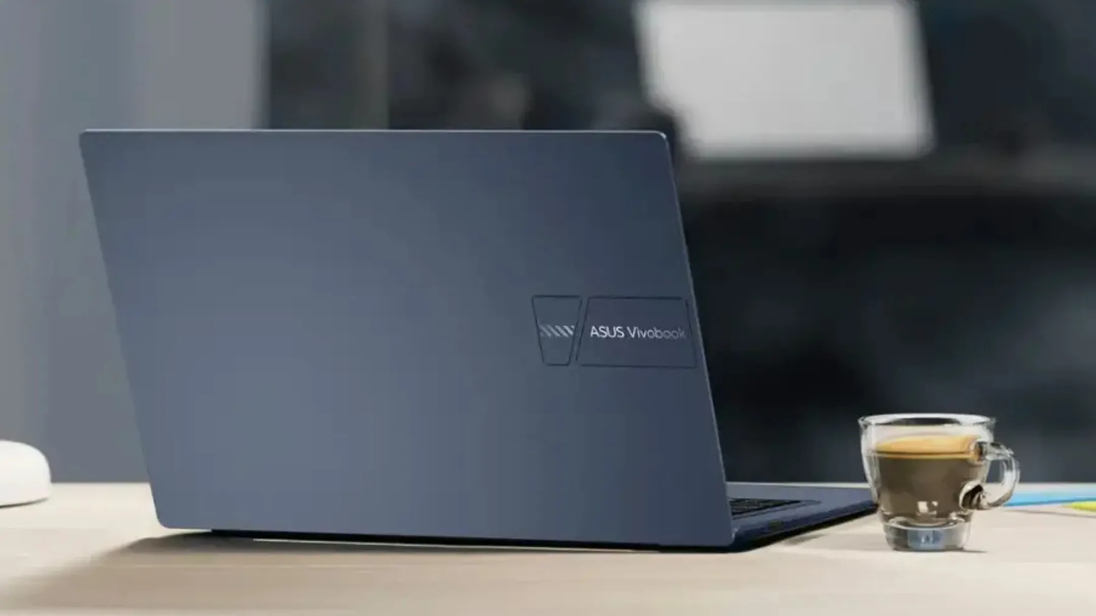 Asus Vivobook 14 trên bàn làm việc cùng cốc cà phê, thể hiện sự tiện lợi cho công việc hàng ngày