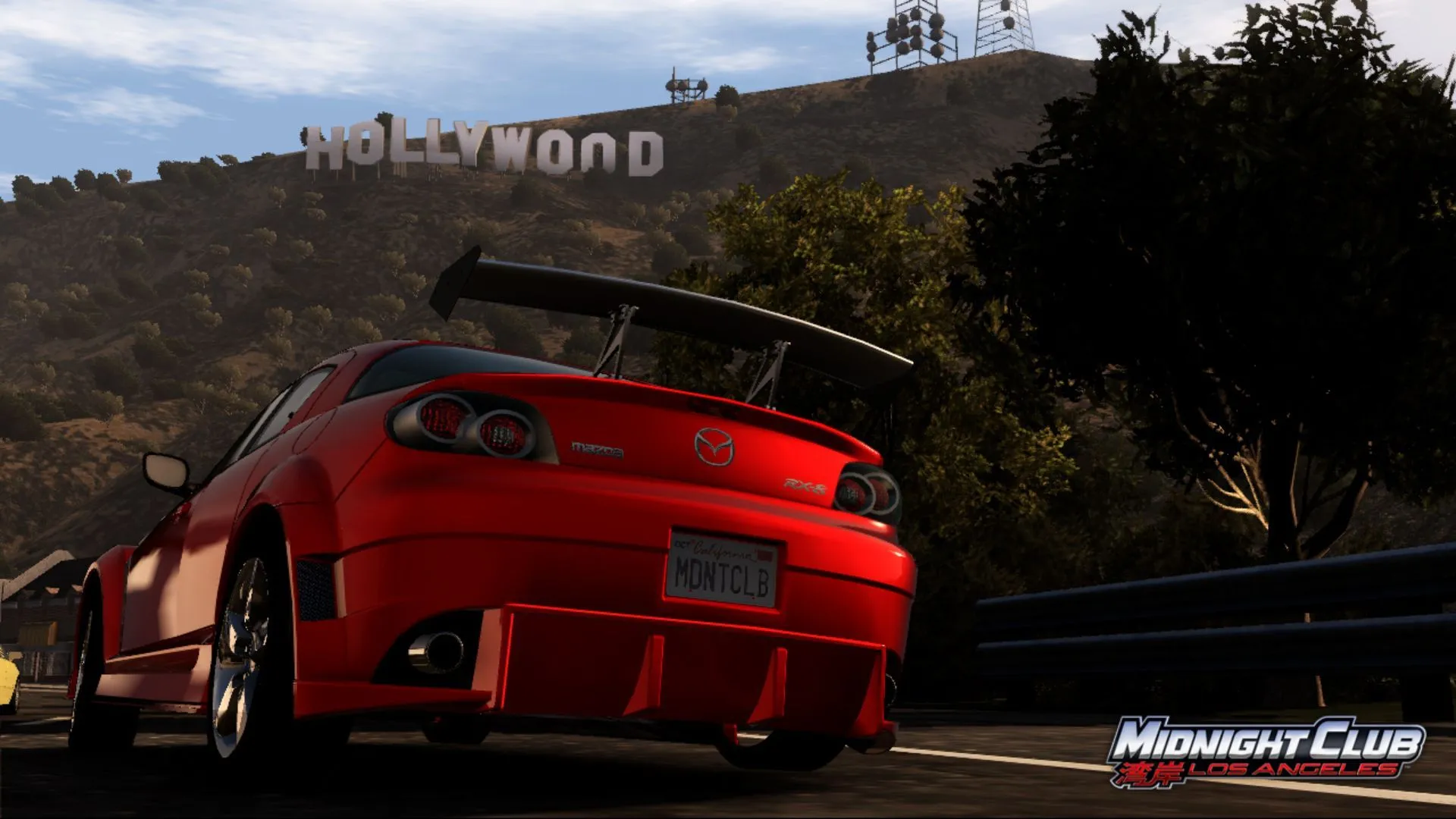 Một chiếc Mazda màu cam đang đua trên đường phố Los Angeles về đêm, phía sau là biểu tượng Hollywood, trong game Midnight Club: Los Angeles.