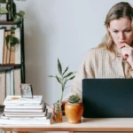 Người phụ nữ trầm tư nhìn màn hình laptop khi ứng dụng theo dõi phần cứng bị gắn cờ malware